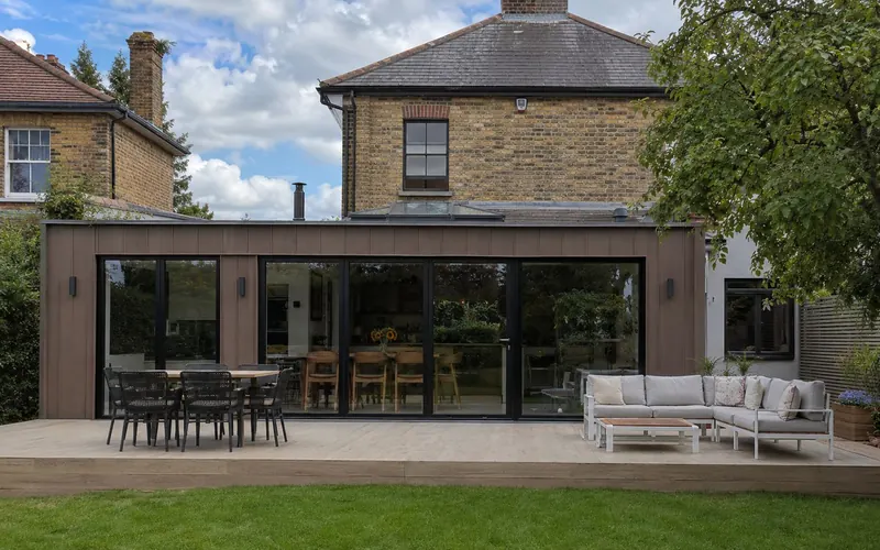A timber-clad rear extension with wide black-framed glazing opening onto a deck and lawn
