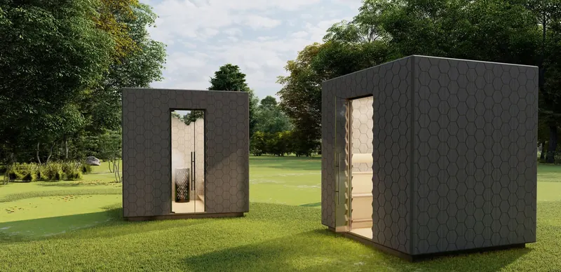 Two dark hexagon-clad garden sauna pods on a lawn among trees