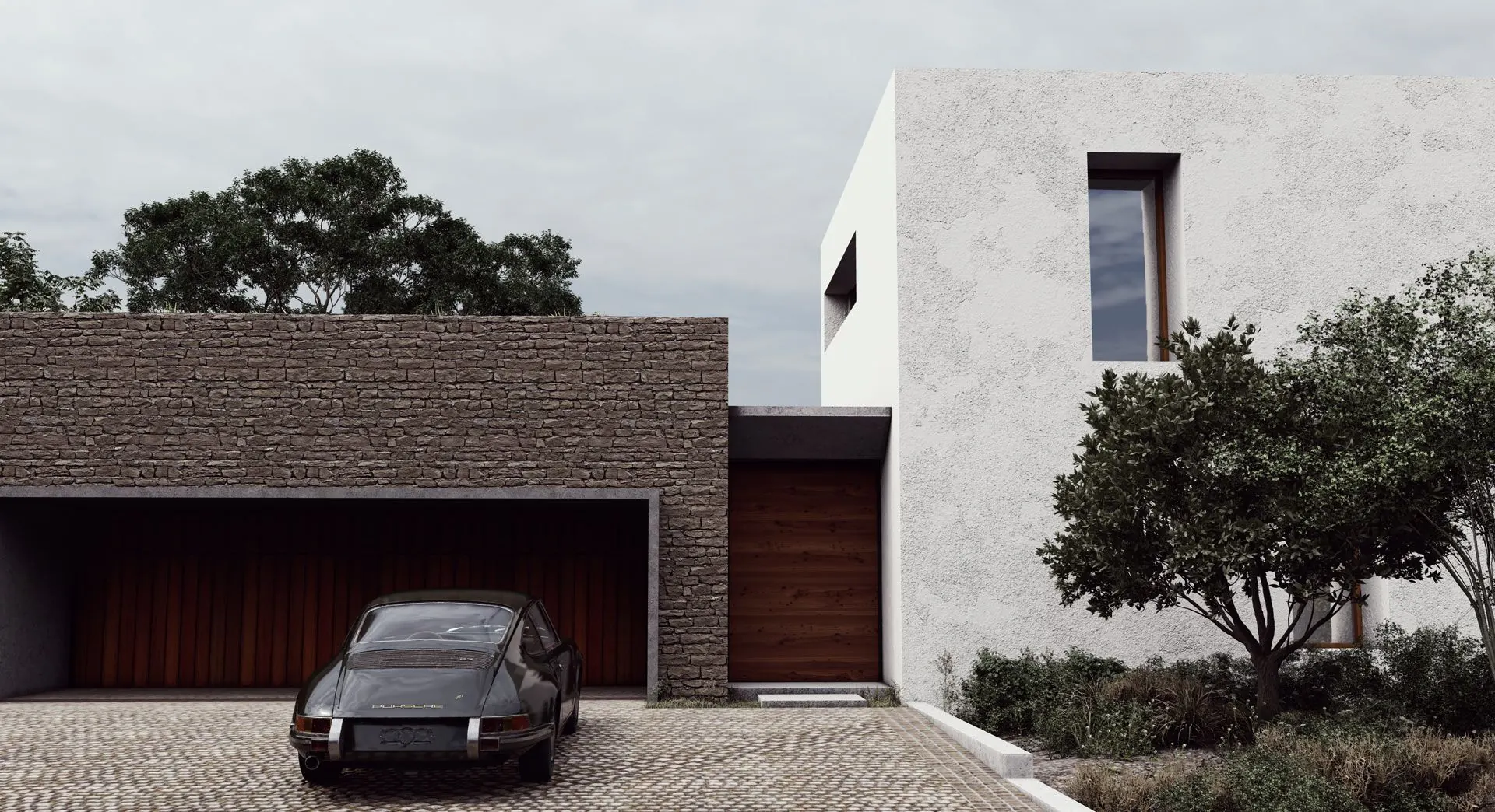A limewashed house beside a dry-stone garage wall, with a timber door and a classic car on a cobbled drive