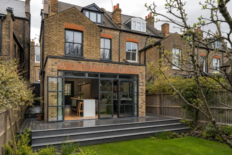 A brick rear extension with black steel-framed glazing and wide grey steps down to the garden